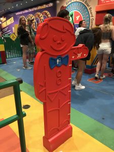 The height measuring stick at Slinky Dog Dash, a flat red plastic cutout of a boy with a blue bowtie and one arm out to the side.