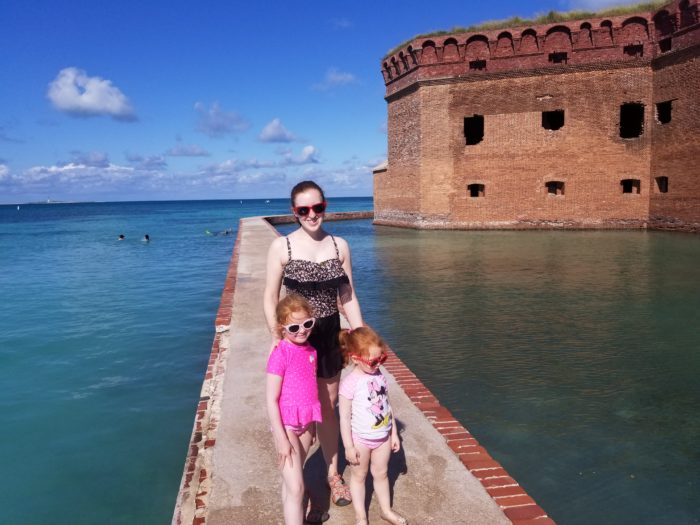 A mom and two daughters stand in swimsuits on a moat wall by a fort in Dry Tortugas National Park