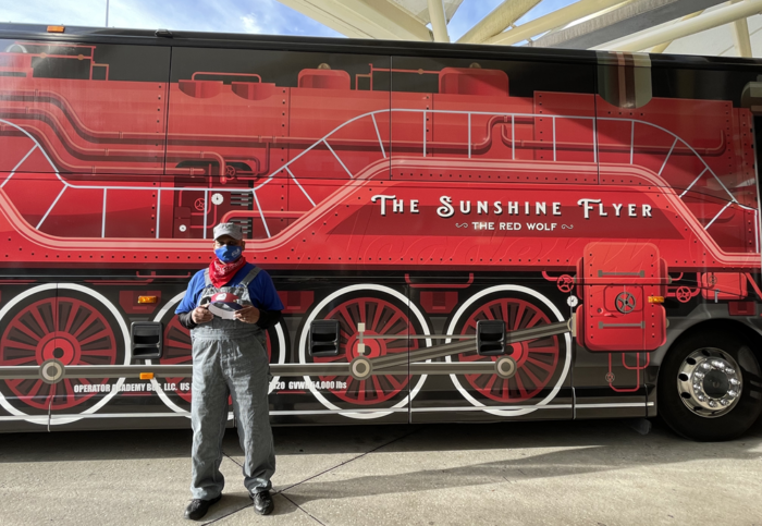 Sunshine Flyer bus wrapped as a red locomotive with driver in front dressed as a conductor.