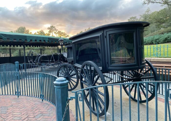 a carriage style hearse with empty traces stands just outside the Haunted Mansion queue
