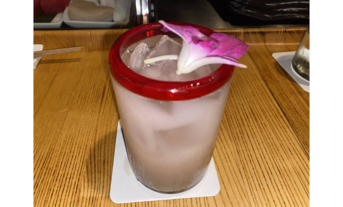 A milky-looking drink in a red-rimmed glass with an orchid on top